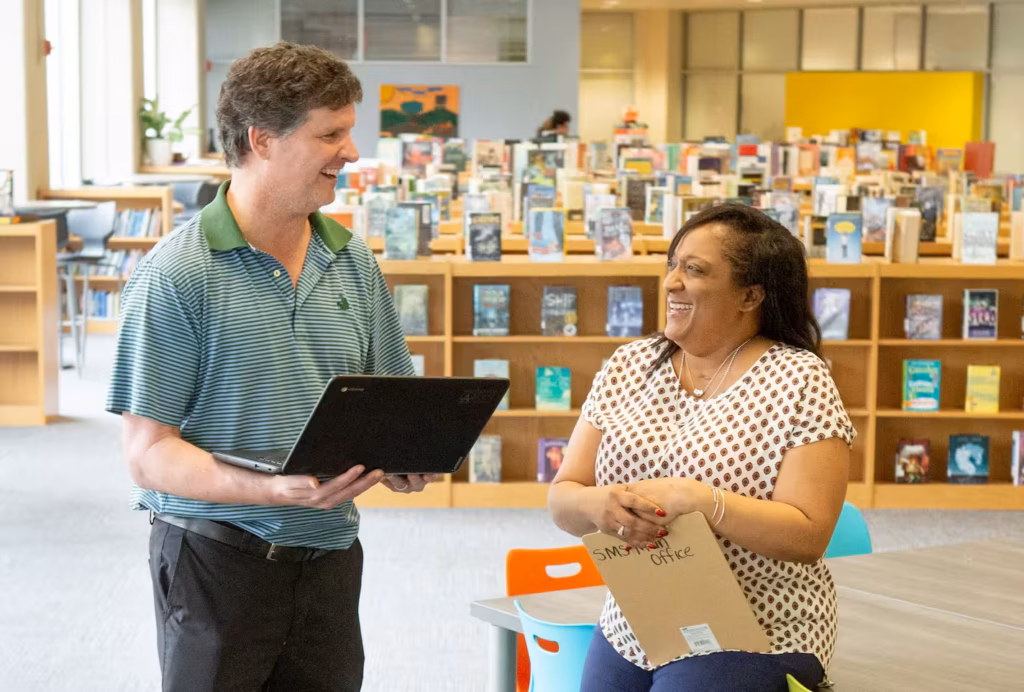 Two teachers standing next to each other in a library.